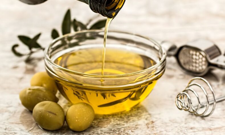 Close-up of olive oil being poured into a glass bowl surrounded by fresh olives and kitchen tools. - Photo by Pixabay on Pexels